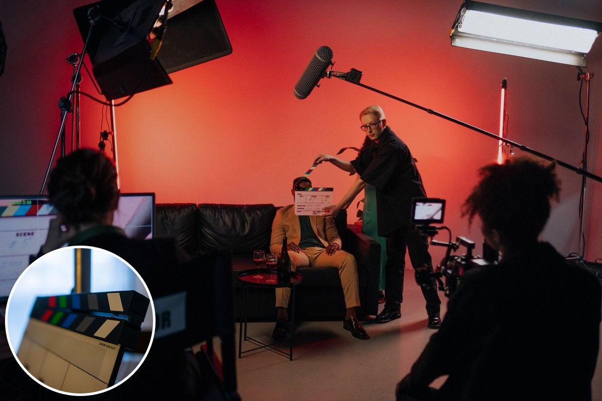A film crew setting up a scene indoors under studio lighting, with a boom microphone and camera rig.
